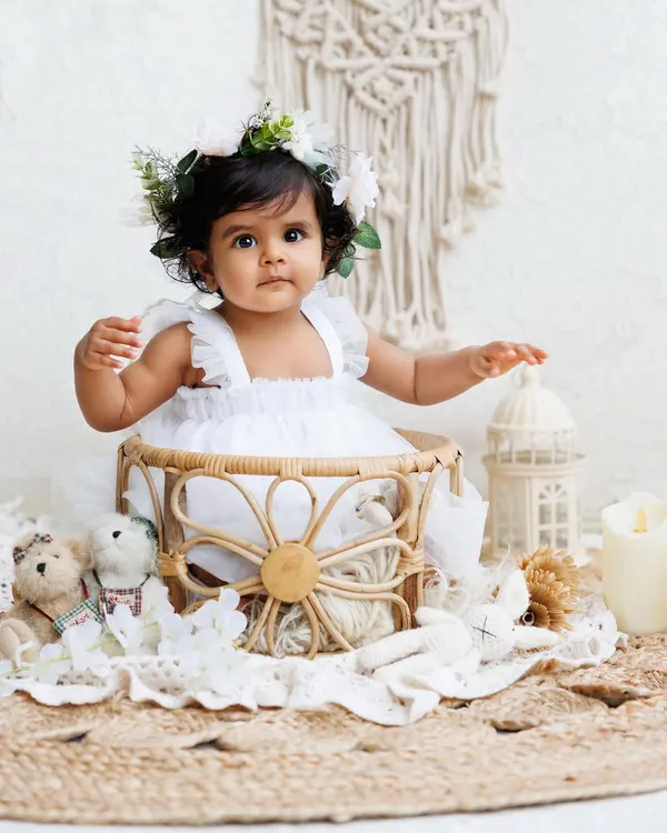 A beautiful baby girl in a white dress and flower crown, sitting in a bohemian-style wicker basket. This theme is simple, elegant, and timeless.