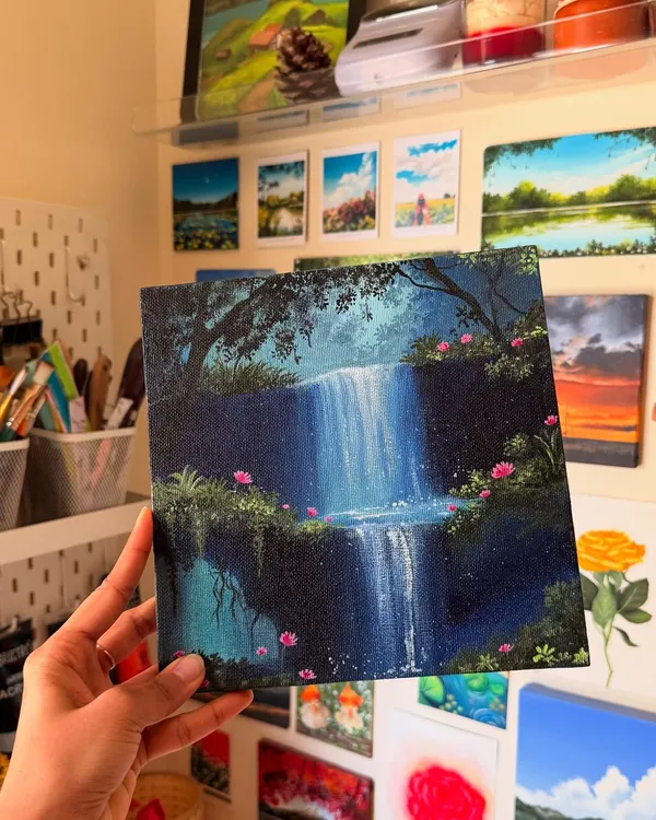 This is a custom acrylic painting of a magical, two-tiered waterfall surrounded by lush greenery and delicate pink flowers. I love creating these fantasy landscape art pieces that feel like they are straight out of a dream.