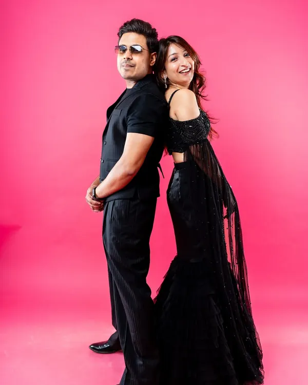A stylish and fun studio portrait of a couple standing back-to-back. Dressed in black against a vibrant pink background, this shot captures their cool confidence and playful connection, making for a modern pre-wedding photo.