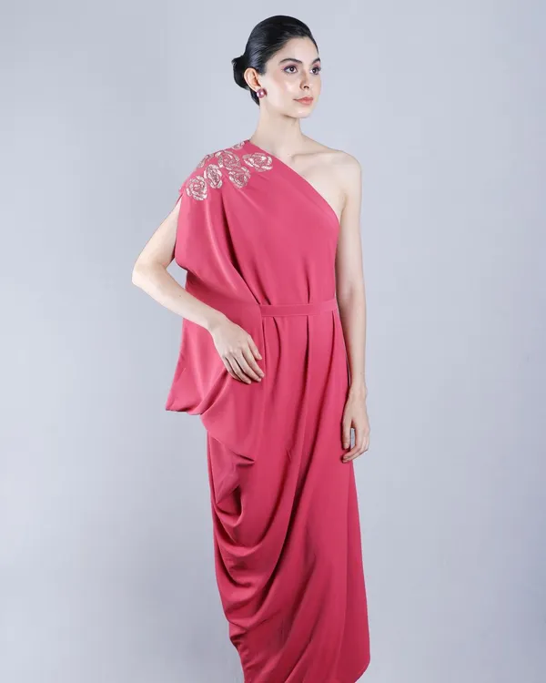 A full-length studio shot capturing the elegant drape and flow of a one-shoulder pink gown, perfect for a designer lookbook or brand campaign.