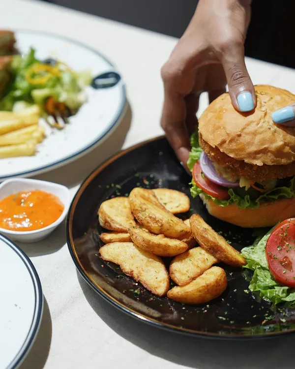 Here is my Ultimate Veg Burger, featuring a crispy patty, fresh lettuce, tomato, and onion in a soft bun. It's served with a side of seasoned potato wedges and dipping sauce.