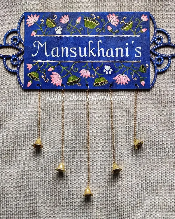 This nameplate features delicate Pichwai-inspired lotus motifs on a deep blue background. The laser-cut MDF base with its ornate edges was also designed by me, and the hanging bells add a final charming touch.