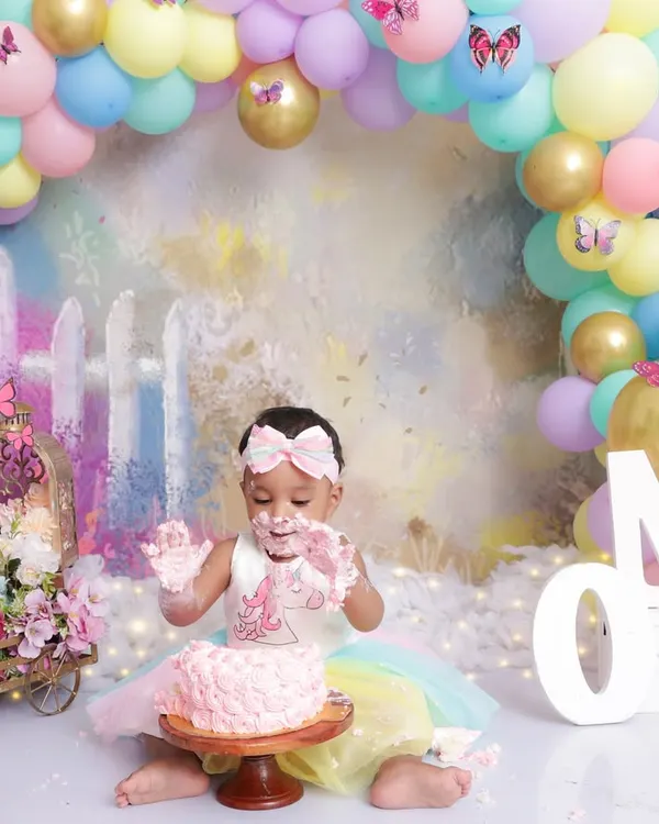 A first birthday cake smash is all about messy fun! This little girl is enjoying her pink cake in a pastel rainbow setup complete with a balloon arch and butterfly details.