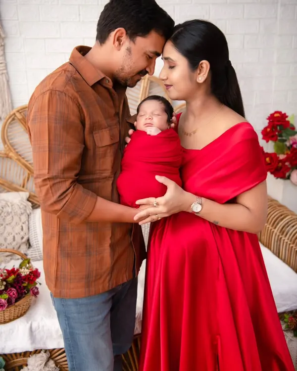 A portrait capturing the profound love of new parents, both gazing at their newborn wrapped in a vibrant red swaddle. This image embodies the beginning of a family's story, a moment of pure connection and adoration that we specialize in preserving.