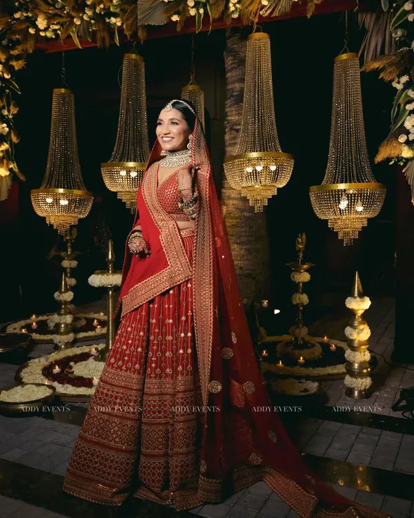 A bride looking like absolute royalty. Dressed in a stunning red lehenga, she is perfectly framed by our opulent decor of grand chandeliers and floral arrangements.