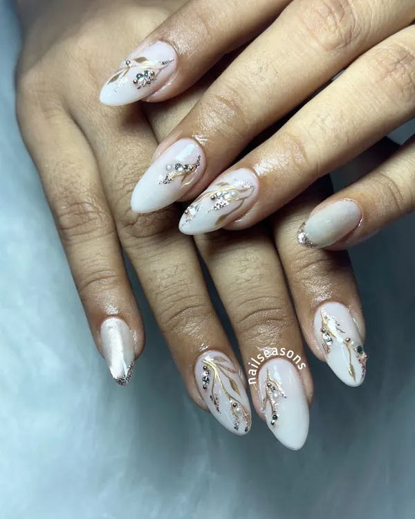An elegant white manicure with hand-painted gold and silver leafy vines, accented with sparkling rhinestones.