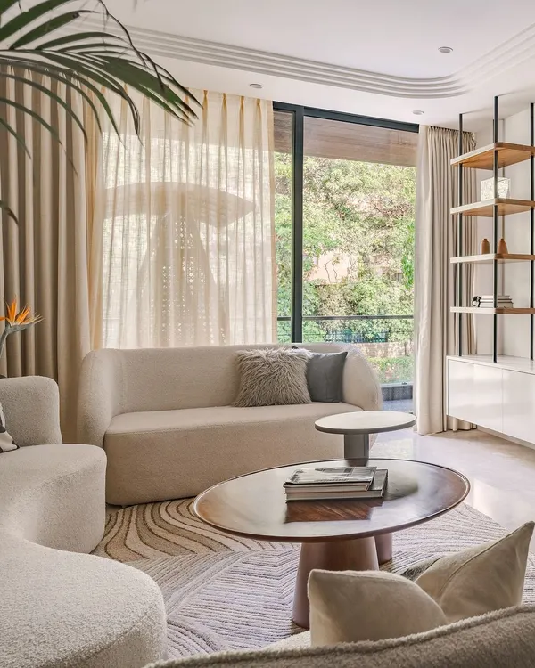 This living room, designed with a Zen-like calm and Wabi-Sabi influences, features curved white sofas that anchor the space. Layered rugs and deep wood coffee tables add texture and warmth, creating a light, airy, and welcoming atmosphere for a young family.