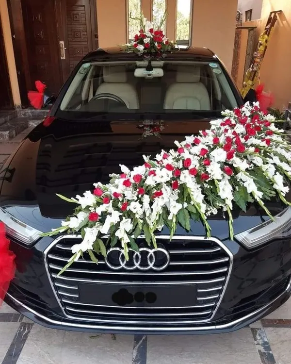 A classic and elegant decoration for a black Audi. The arrangement features a cascade of white gladiolus and red roses across the bonnet, with matching red ribbons on the side mirrors for a complete look.