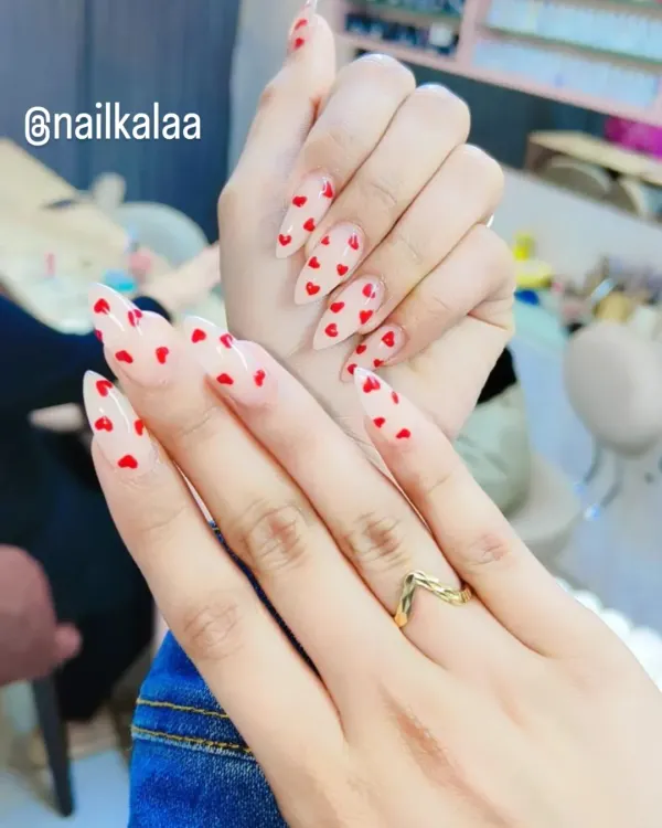 A sweet and romantic design featuring tiny, hand-painted red hearts scattered over a sheer nude base on long stiletto nails.