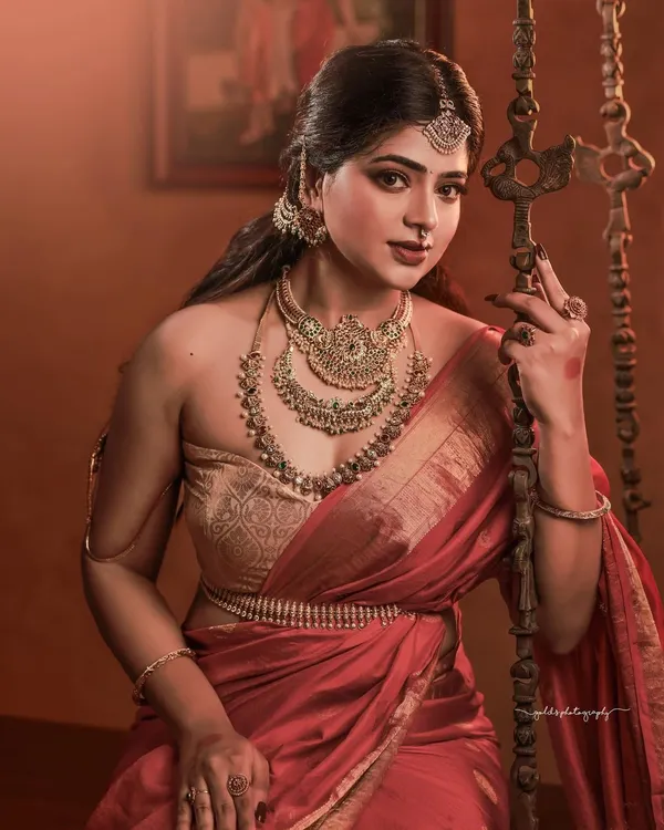 A portrait that feels like a classic painting. The composition, with the bride seated by a traditional swing in a heritage home, combined with the rich red saree and antique gold jewelry, creates a powerful and regal image.