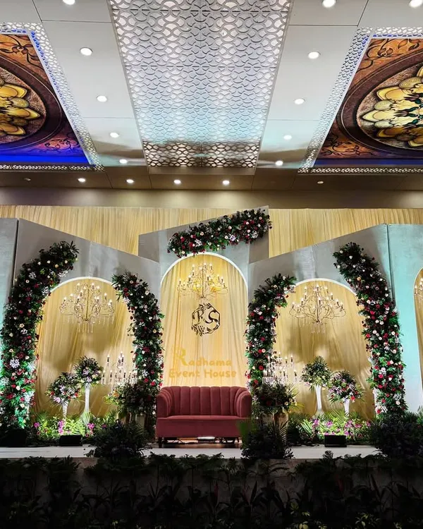 A breathtaking reception stage featuring Roman-style arches, cascading floral arrangements, and elegant chandeliers. The design complements the venue's ornate ceiling, creating a cohesive and luxurious look.