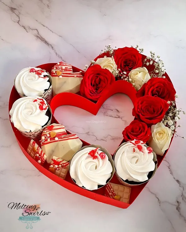 Our Valentine's Day heart hamper is the perfect romantic gift. This beautiful heart-shaped box is filled with fresh red and white roses, decadent cupcakes, and geometric white chocolate hearts.