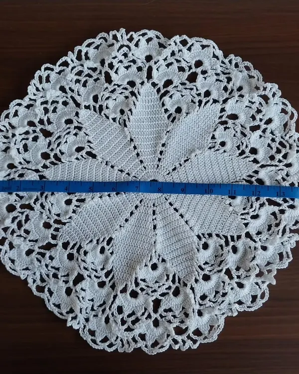 A large, 15-inch white crochet doily with a beautiful star-like pattern. I'm showing the size with a measuring tape. It's perfect as a statement table centerpiece.