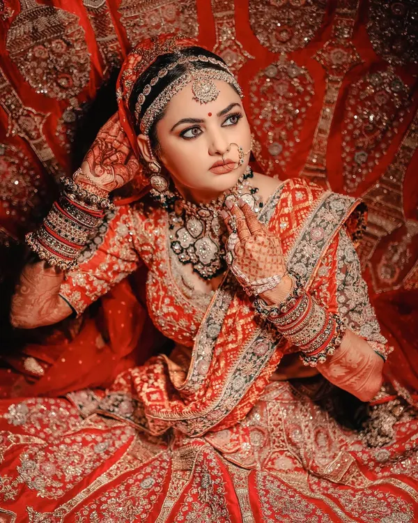 A truly classic bridal portrait. The bride's pose, her stunning red and gold lehenga, and the intricate details of her jewelry are all highlighted to create an image of timeless Indian bridal beauty.