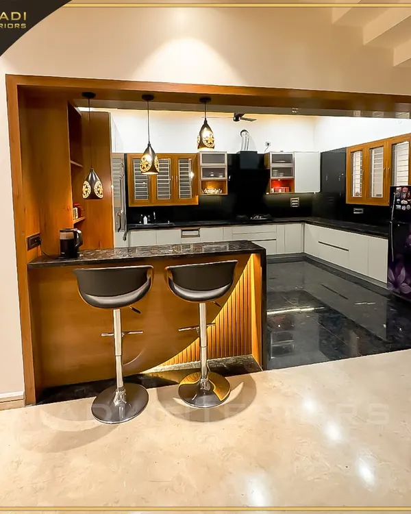 An open-concept kitchen with a stylish breakfast bar and modern stools. The design features a mix of wood and white cabinets, black granite countertops, and elegant pendant lighting.