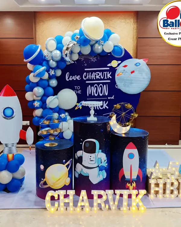 A stellar space-themed fifth birthday party. This setup features a "Love you to the moon and back" backdrop, a rocket ship balloon sculpture, and astronaut-themed plinths.