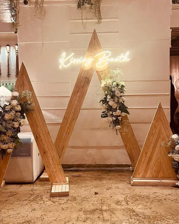 This custom-designed wooden arch with a "Kissing Booth" neon sign was the highlight of a 25th-anniversary celebration. It served as a perfect photo opportunity, blending rustic charm with modern elegance.