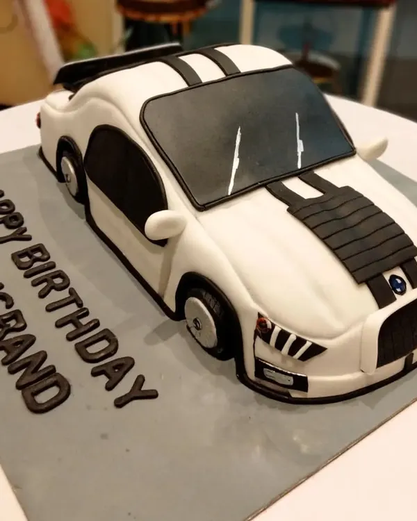 A fully sculpted 3D sports car cake, custom-made for a husband's birthday. Every curve and detail of the car is carved and decorated by hand to create a realistic and impressive centerpiece.