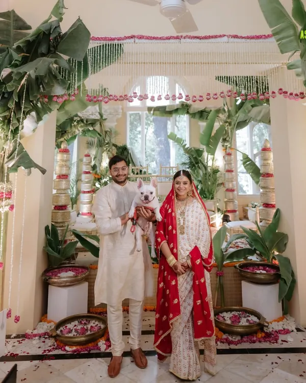 An intimate home wedding, where the couple stands with their furry friend in front of a beautiful, minimalist mandap made with banana leaves and tuberoses.