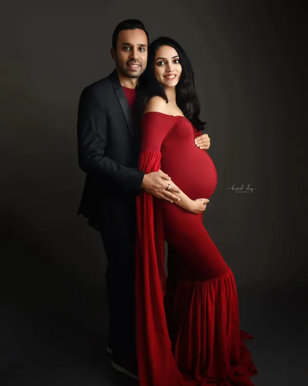 A dramatic studio maternity portrait featuring a stunning red gown against a dark backdrop. This classic, formal style creates a powerful and elegant image.
