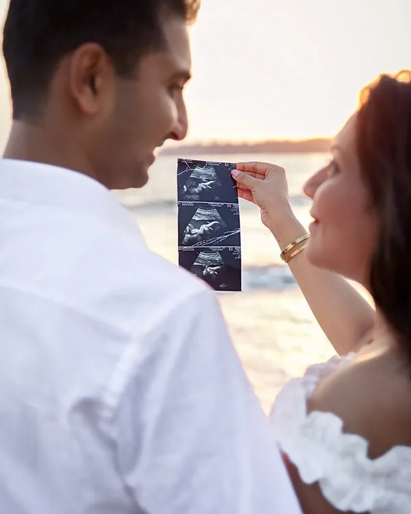 A close-up of the first family photo. Using your ultrasound scan during a beach sunset shoot is a deeply personal and beautiful way to announce your pregnancy.