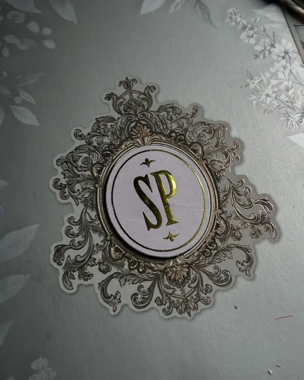 This is what I mean by a signature story. A close-up of a custom 'SP' monogram, crafted with gold foil and surrounded by an intricate, vintage-inspired silver emblem.