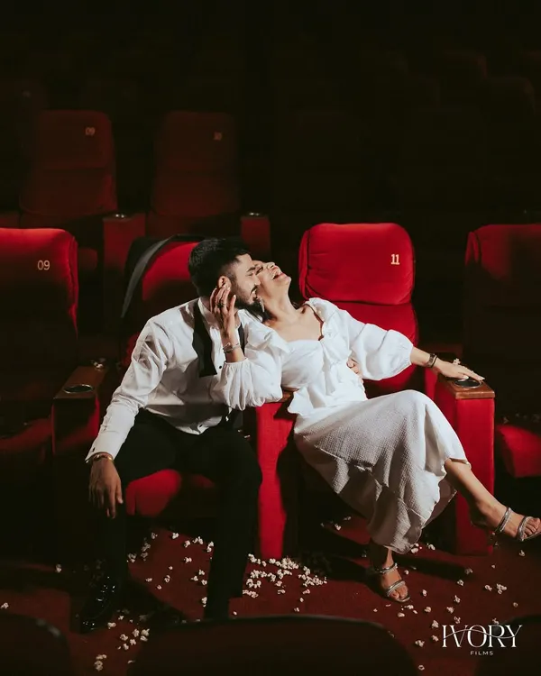 A moment of pure, unscripted joy during a unique pre-wedding shoot in an empty theatre. The dramatic red seats and scattered popcorn set the stage, but their genuine laughter is the real story here, showcasing a love that's playful and real.