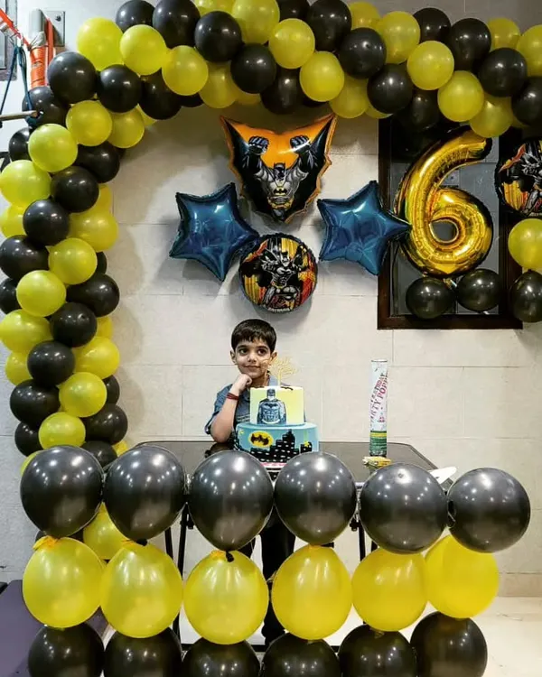 The birthday boy posing with his Batman-themed cake in front of a matching black and yellow balloon arch. We go all-in on creating the perfect superhero headquarters for your child's special day.