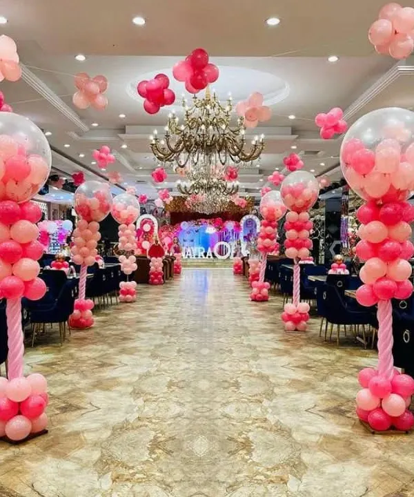 A grand hall decorated for a party. This setup includes large balloon pillars with bubble balloon tops, creating an elegant and festive walkway for guests.