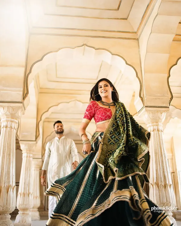 A vibrant shot of a bride in a traditional green bandhani lehenga, her joyful expression captured as she walks through a palace corridor in Jaipur.