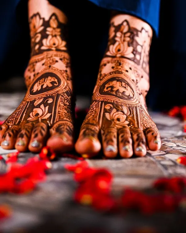 Beautifully captured bridal feet mehendi, adorned with lotus and elephant motifs and surrounded by delicate rose petals.