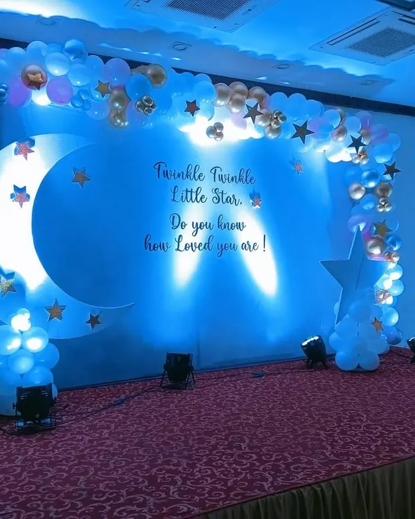 A dreamy "Twinkle Twinkle Little Star" baby shower theme with a large crescent moon prop and a cloud-like balloon arch.
