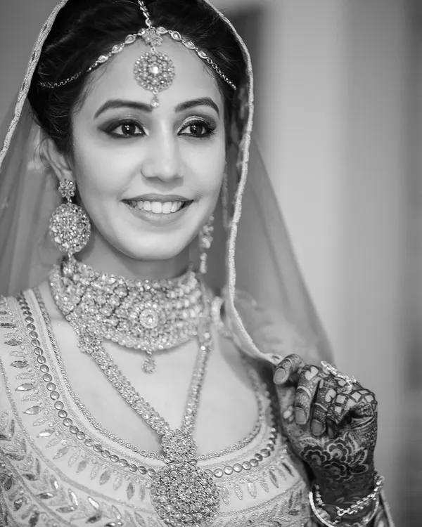 A radiant black and white bridal portrait that captures a genuine smile. Monochrome photography strips away color to focus on emotion, light, and the exquisite detail of the wedding jewelry and henna.