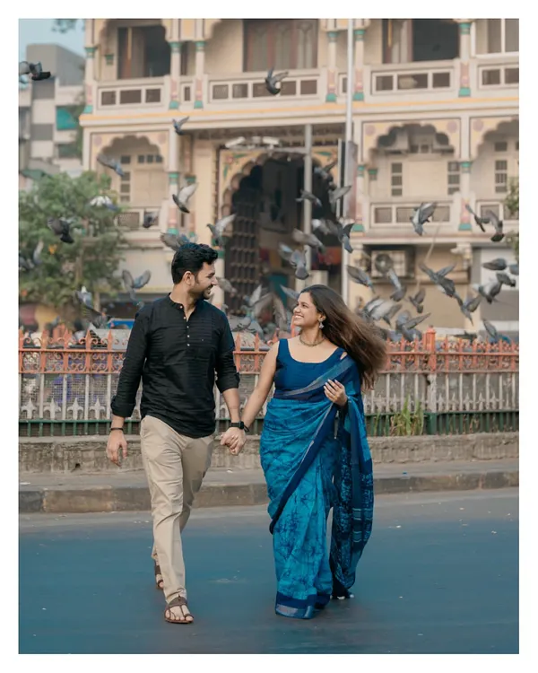 A classic Mumbai pre-wedding shot, capturing the couple walking hand-in-hand as pigeons take flight around them.