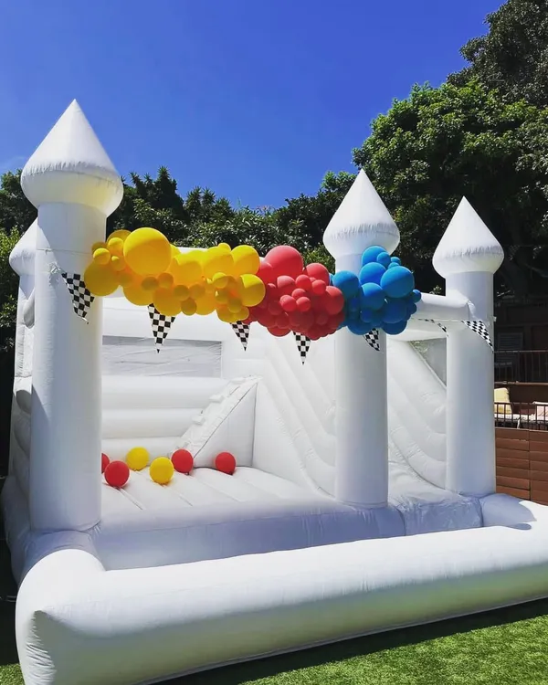 Our elegant white bouncy castle, shown here with a slide and ball pit, is a versatile choice for any event, from birthdays to more formal gatherings. It can be decorated with balloons to match your party's theme.