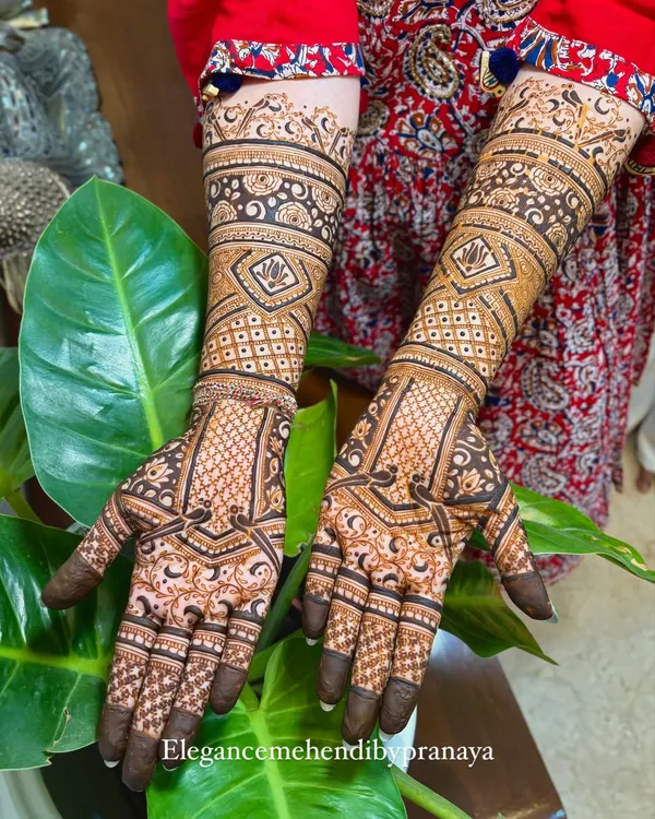 A beautiful, dense bridal mehendi with a mix of geometric checks, floral bands, and delicate details covering the hands and arms.
