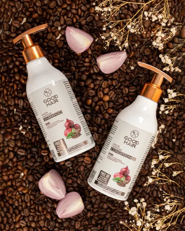 This top-down flat lay of shampoo and conditioner bottles is arranged on a bed of coffee beans with onion slices. This visually connects the products directly to their main ingredients, telling a clear story about the formula.