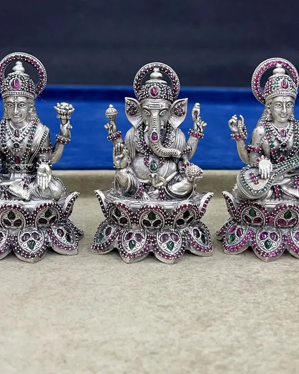 The complete set of our 925 silver Lakshmi, Ganesh, and Saraswati idols. The intricate stone work in ruby and emerald on the crowns and lotus bases highlights the divine details of each deity.