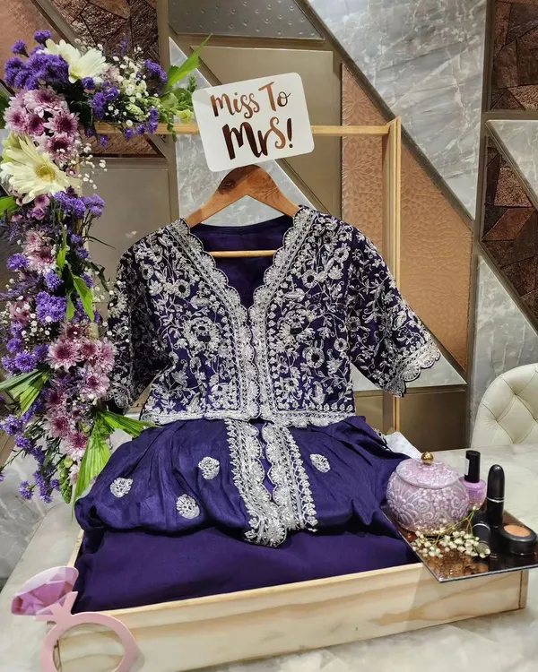 We love creating the perfect presentation for a bride's new journey. This trousseau display features a custom wooden stand with a mini hanger for the outfit, surrounded by a lush arrangement of fresh purple and white flowers, and a fun 'Miss to Mrs!' sign to complete the look.