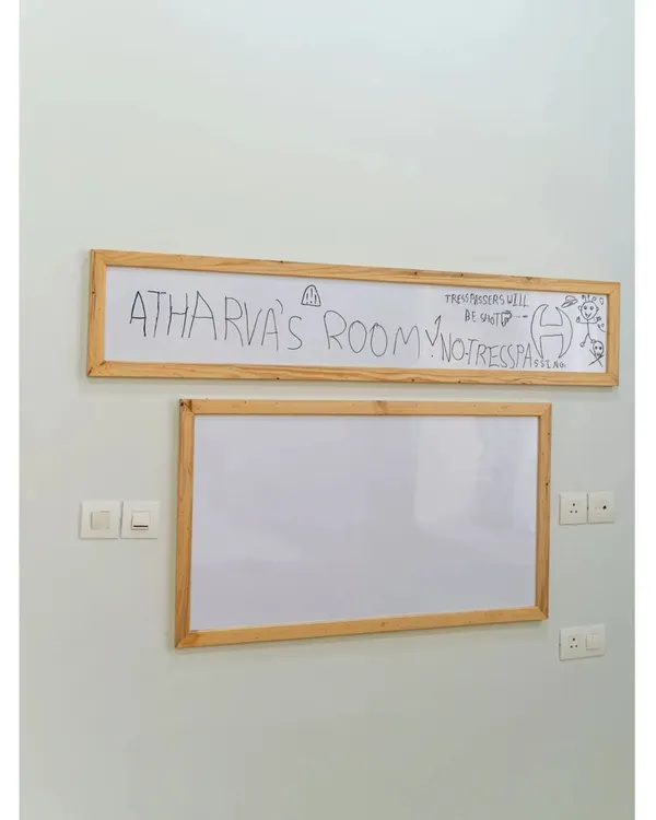 A room truly claimed by its owner! This custom whiteboard with a wooden frame proudly announces "Atharva's Room," serving as a canvas for his creativity and a fun, personal touch to his space-themed bedroom.