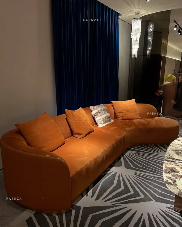 This custom-designed curved sectional sofa, upholstered in a bold orange velvet, becomes the vibrant heart of the living room. The quilted detailing on the arms adds a layer of texture and sophistication, creating an inviting space for conversation and relaxation.
