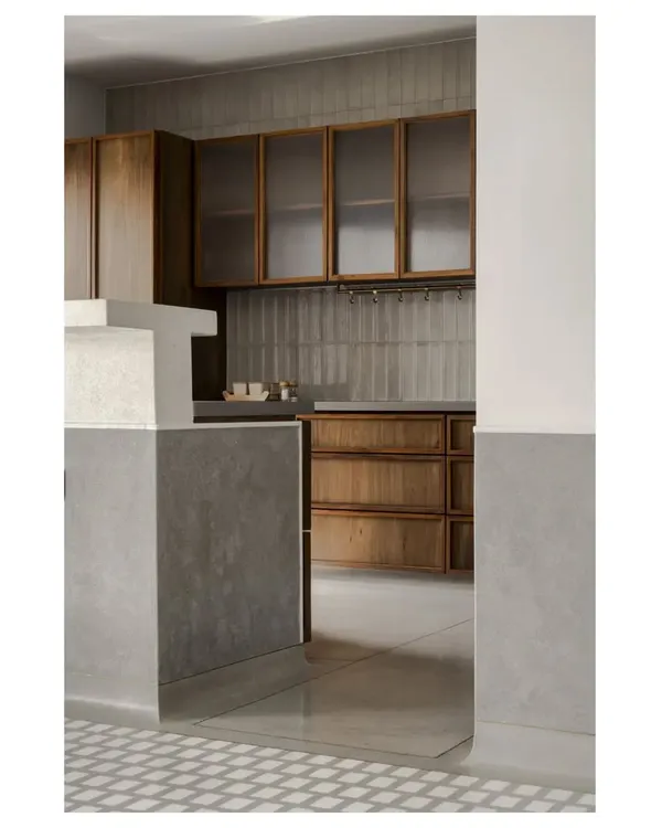 A glimpse into the kitchen of 'A Home Set in Stone', where the cool grey of the in-situ terrazzo floor meets the warm teak of the cabinetry. The frosted glass and handmade tiles add another layer of texture.