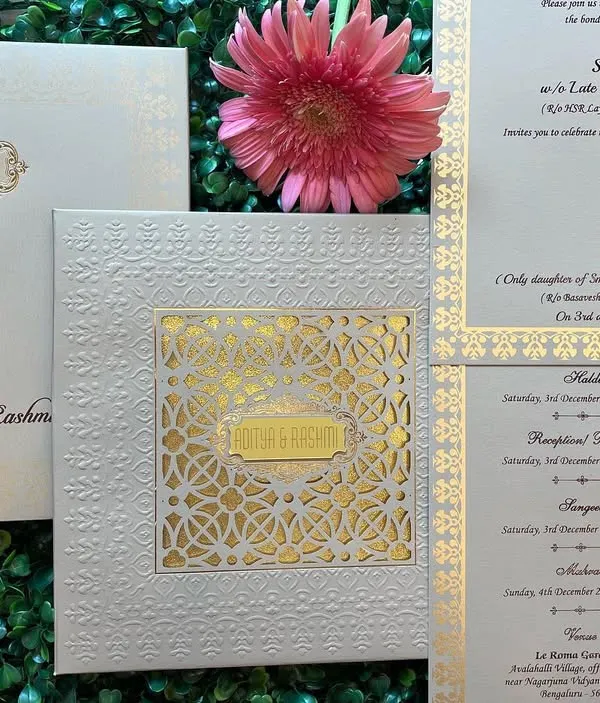 A classic and sophisticated wedding invitation set in white and gold. This design features a laser-cut sleeve over a gold foil base, with separate, well-organized inserts for the different wedding programs like Haldi, Sangeet, and Reception.