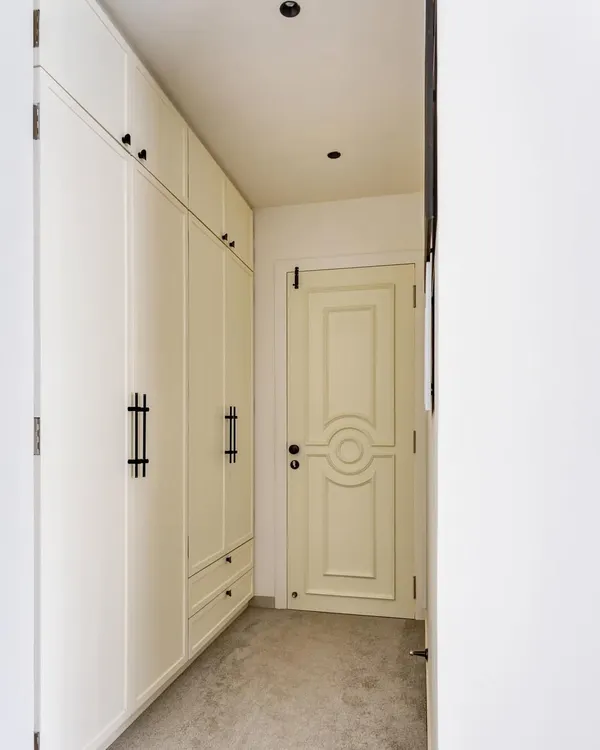 The master bedroom's walk-in wardrobe features clean, white paneled doors and elegant black handles, leading to a beautifully detailed bedroom door. This corridor is a perfect example of our focus on creating seamless and sophisticated transitions between spaces.