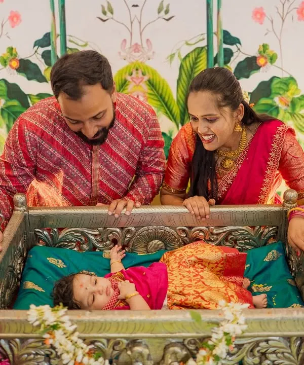 A cherished moment from a naming ceremony, where the parents gaze lovingly at their newborn resting in a beautifully decorated traditional jhoola, or cradle.
