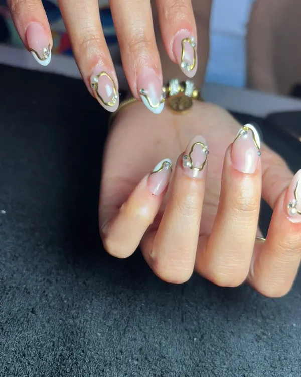 A beautiful and abstract design featuring 3D gold lines and small pearls over a sheer nude base. This is a very trendy "gold jewelry" nail look.