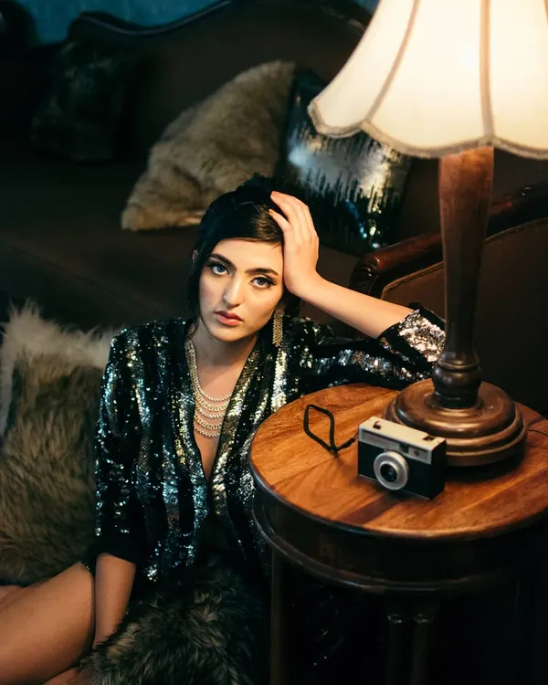 A vintage-inspired indoor portrait using a single lamp and on-camera flash to create a moody, cinematic scene. The props and styling add to the old-world elegance of this dramatic shot.