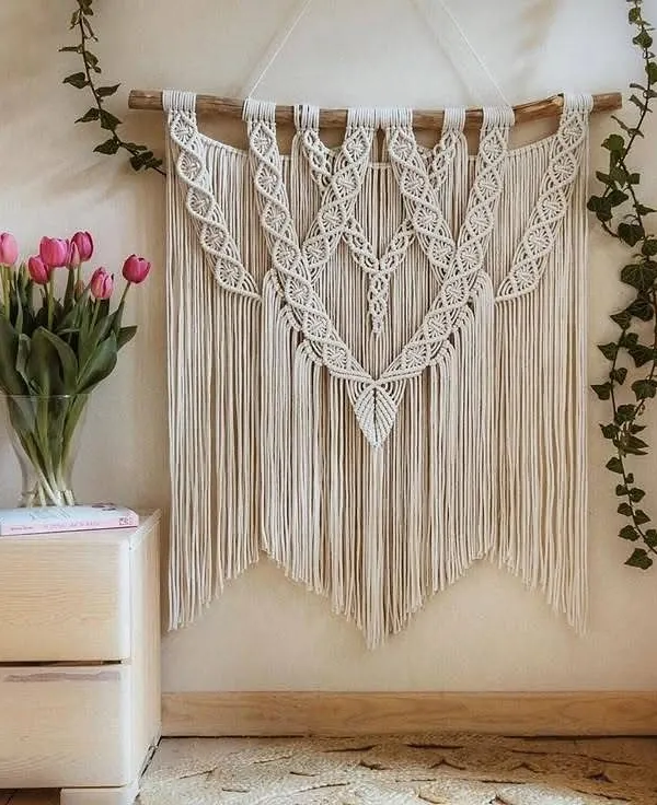 A large, elegant macrame wall hanging styled beautifully above a wooden side table with fresh tulips. This shows how my art can elevate a space and create a serene, boho-chic atmosphere.