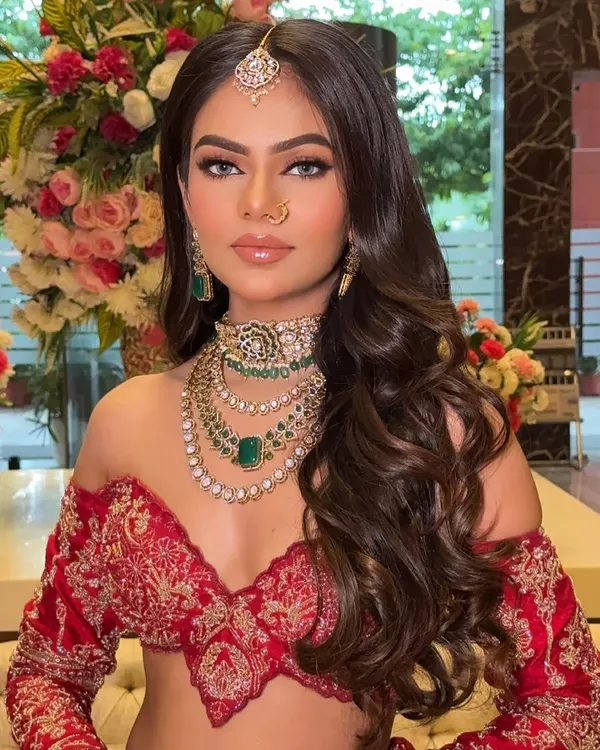 A stunning royal red bridal look. The focus is on a flawless full-coverage base, smoked-out kohl eyes, and glossy nude lips for a modern yet regal feel.