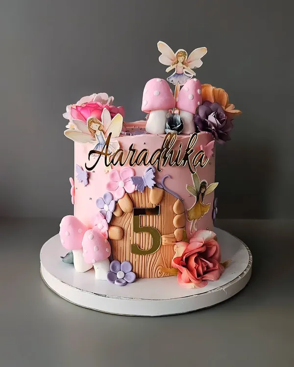 A magical fairy theme cake for Aaradhika's 5th birthday. This butterscotch cake features a fairy house with mushroom details, delicate wings, and whimsical flowers.